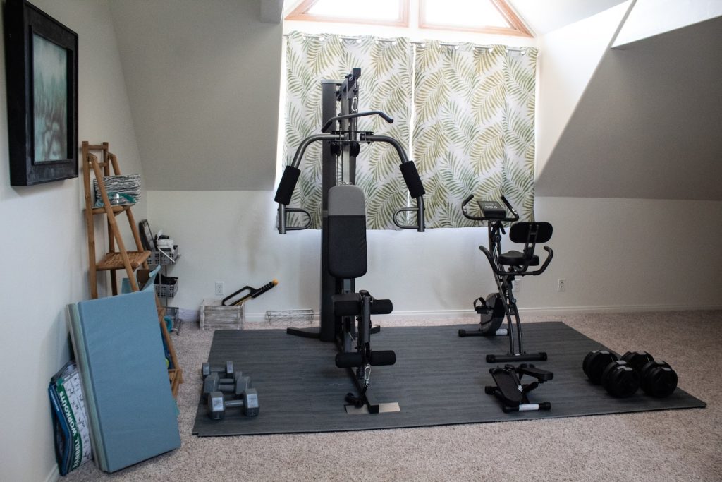Home gym setup with exercise bike, weights, and home gym machine in a cosy room with bright windows