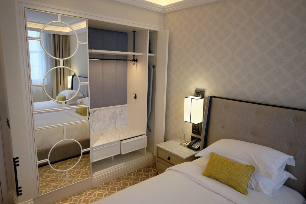 An elegant hotel room with a bed, mirror, nightstand, and modern decor, featuring soft lighting and a cosy atmosphere