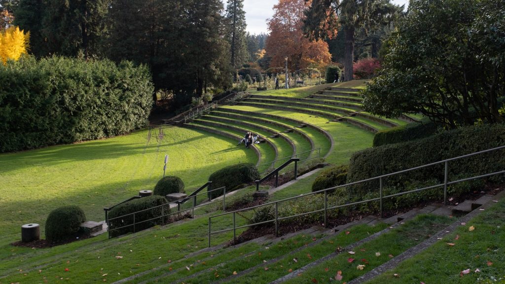 Serene park amphitheatre with green terraces, surrounded by lush trees and a couple enjoying the tranquil scenery