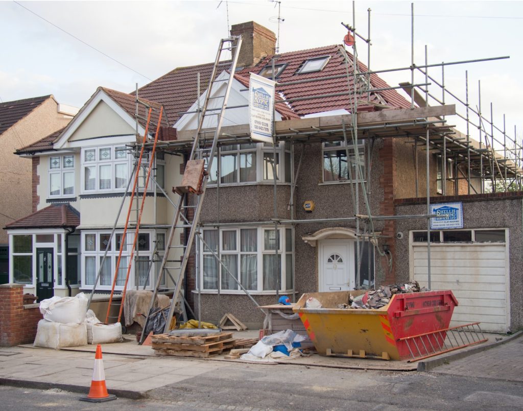 House under renovation with scaffolding and skip, construction materials on driveway, red-tiled roof in progress