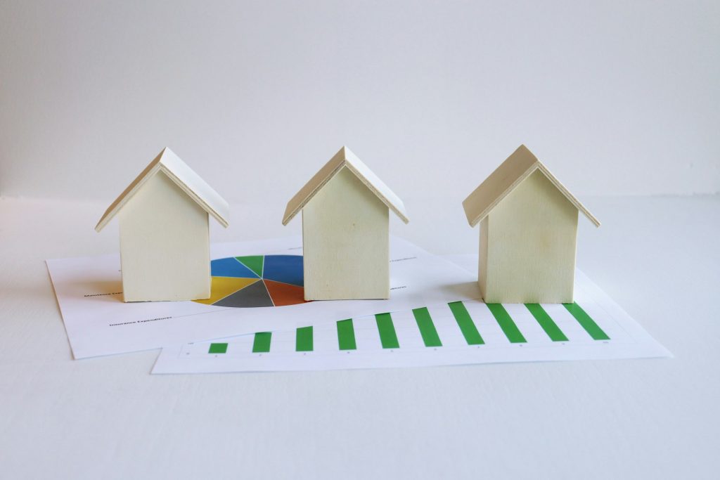 Three wooden house models on financial charts, highlighting real estate market trends and analysis